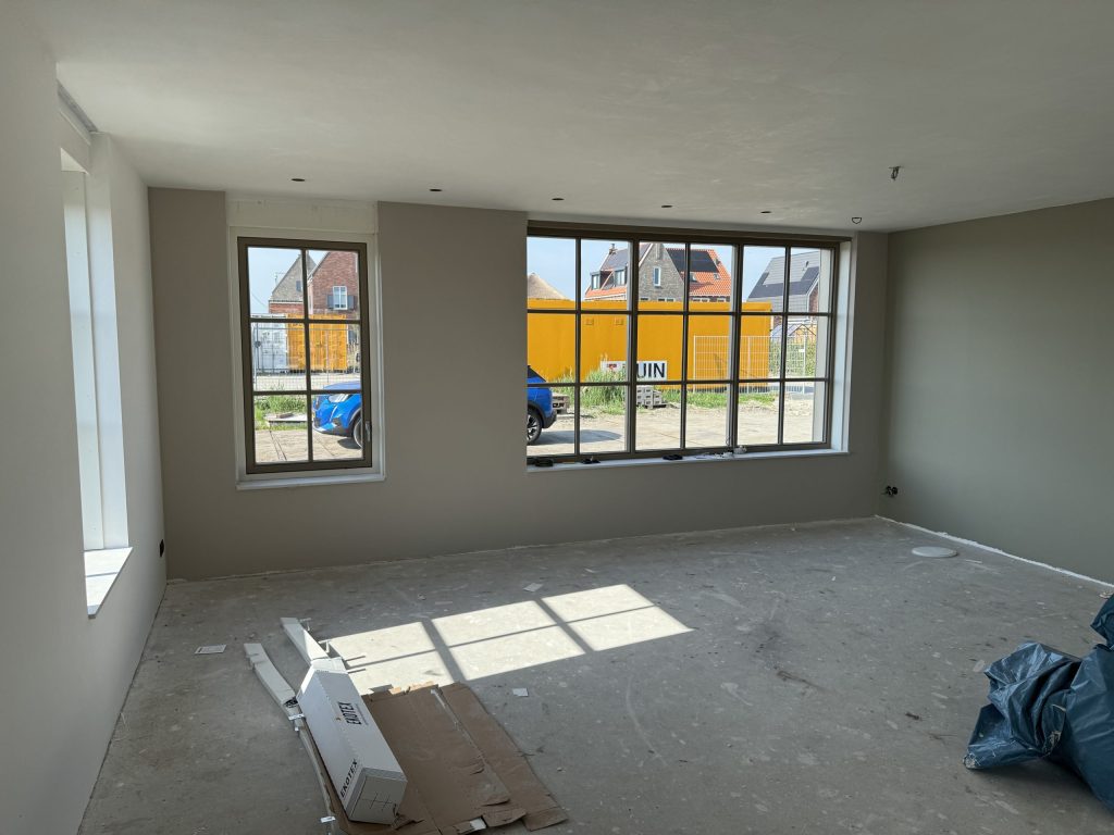 Nieuwbouwwoonkamer met wanden in een warme grijstint en een groot roedenraam aan de straatkant